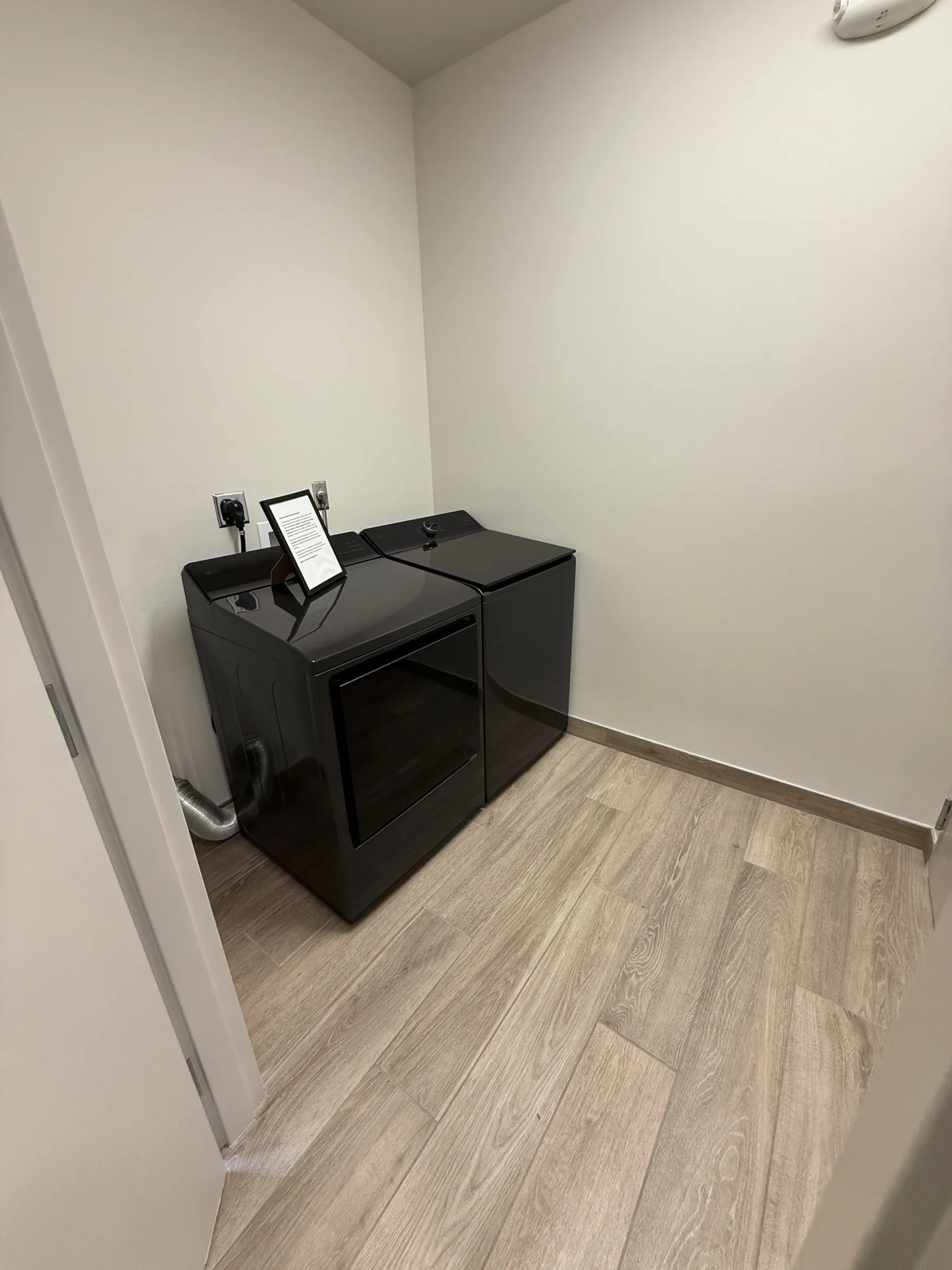 Laundry room with a black top-load washer and dryer pair in the corner over plank flooring.