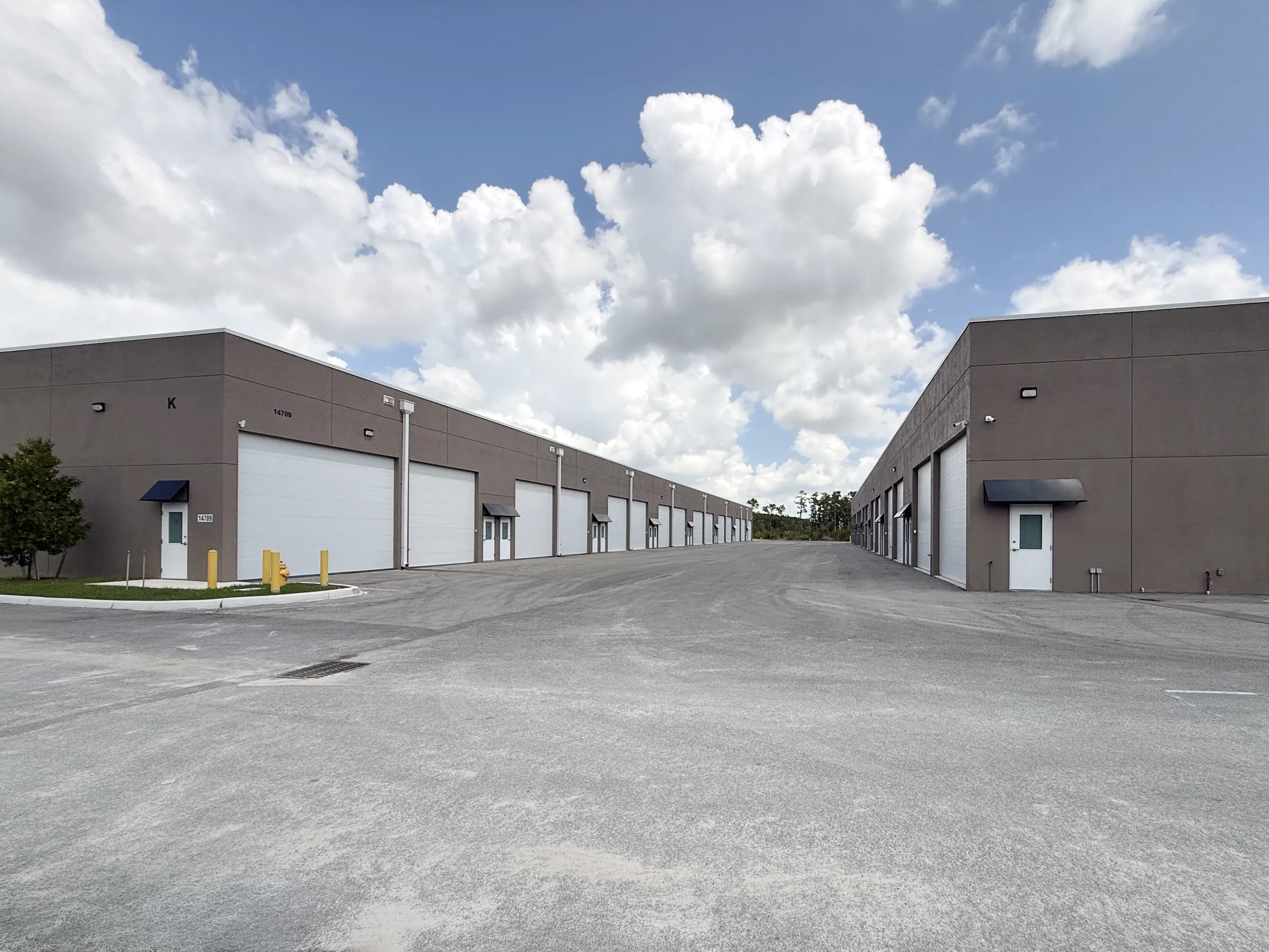 Wide ground-level view down the paved drive aisle between two long buildings lined with white garage doors, dramatic clouds overhead.