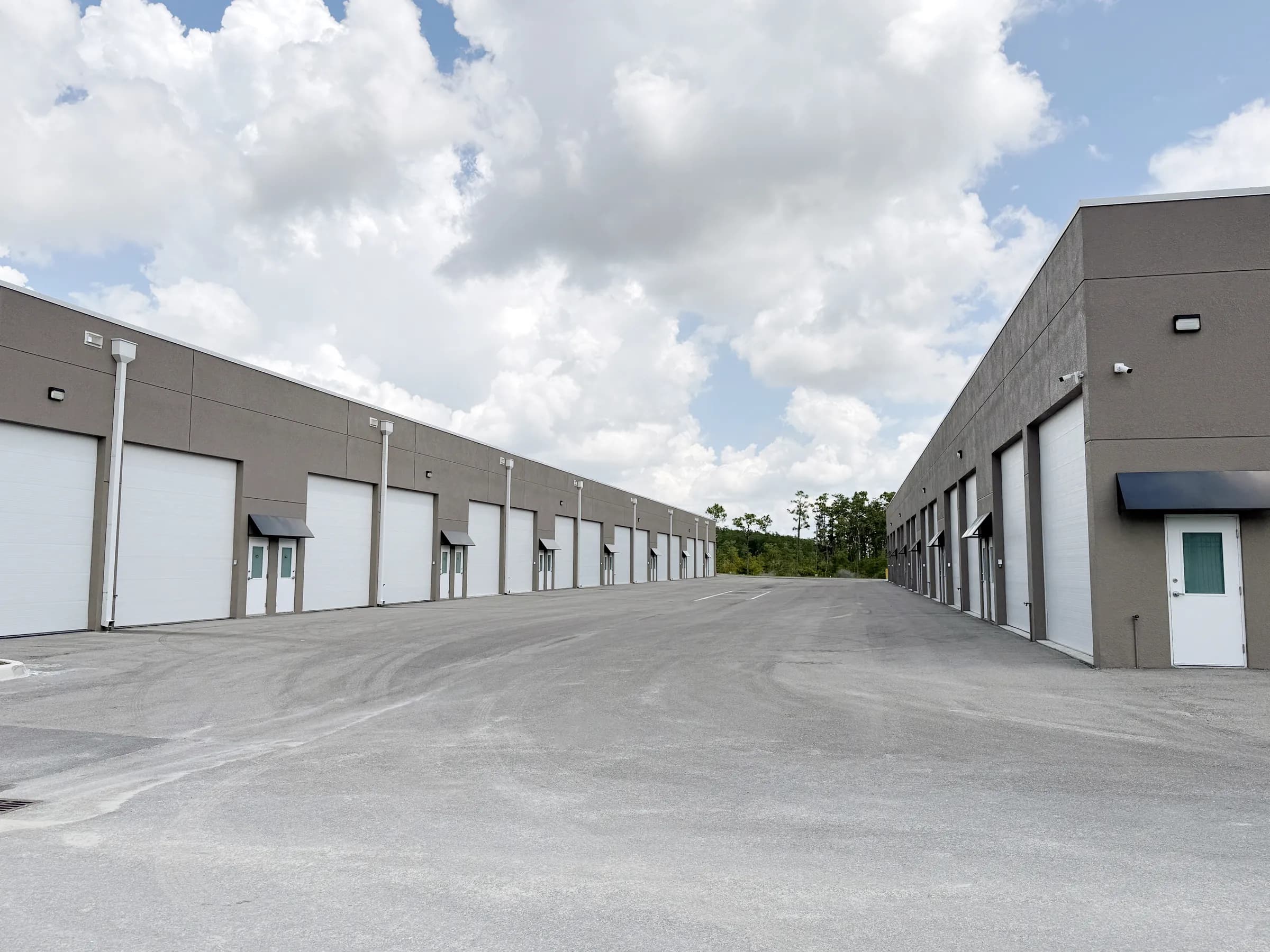 A second drive-aisle view flanked by two rows of tan buildings with white overhead doors under a partly cloudy sky.