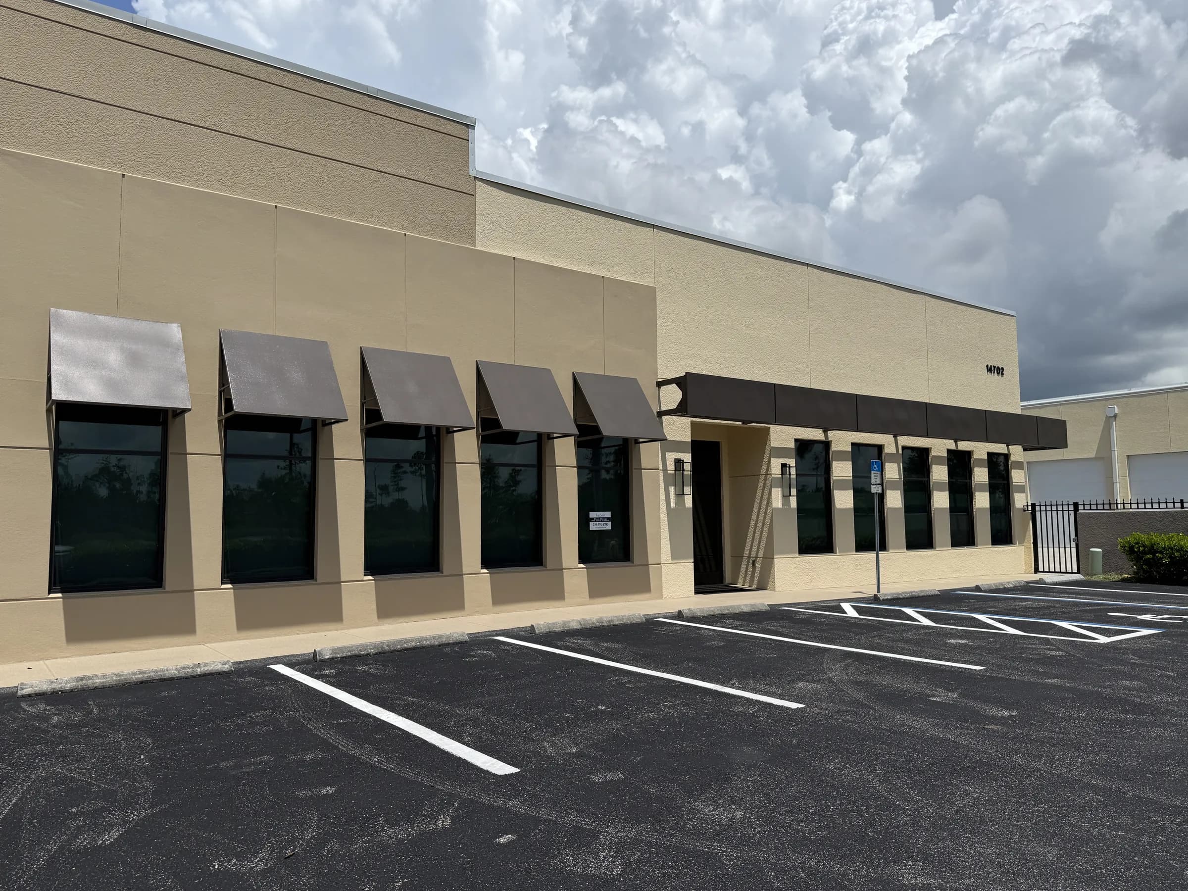Angled view along the office facade — five bronze awnings over dark tinted windows above striped parking spaces.