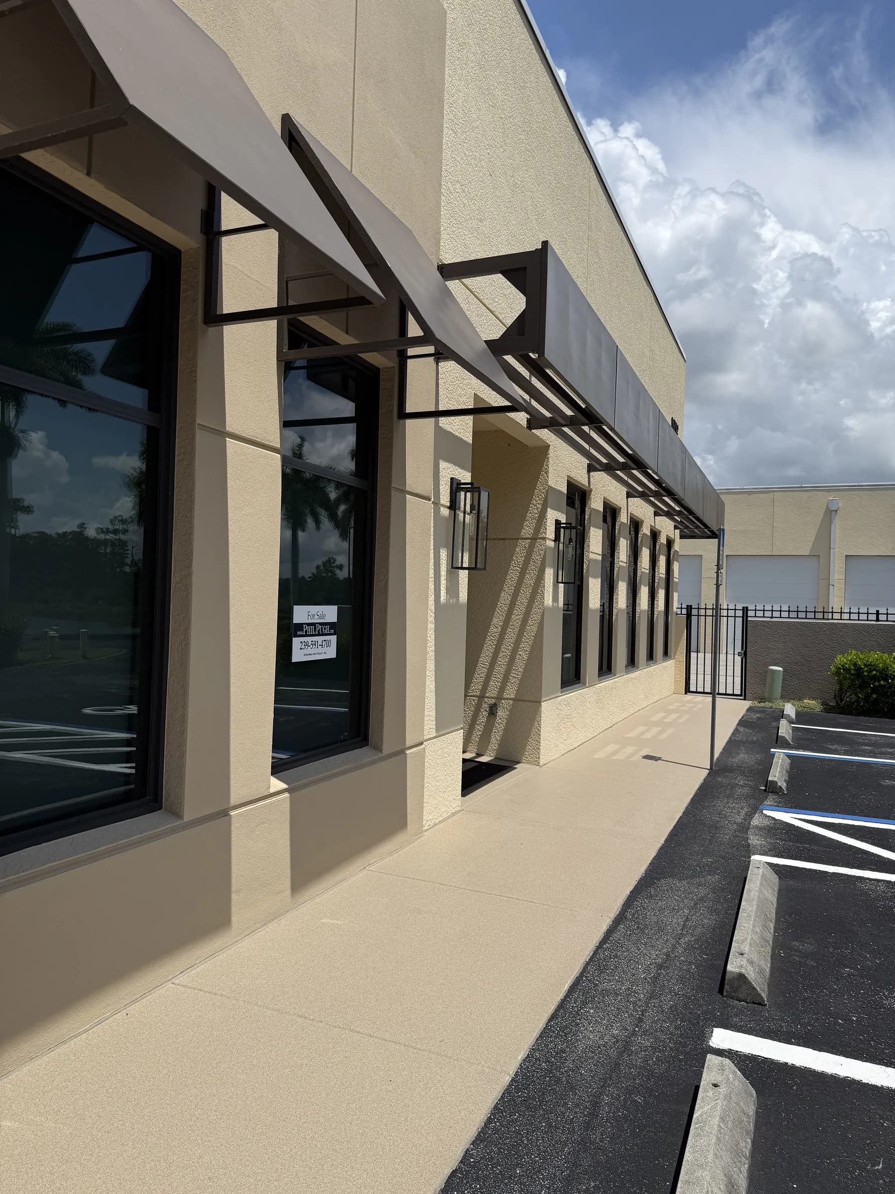 Steep perspective down the office wall, the run of bronze awnings receding toward the gate over a wide sidewalk.