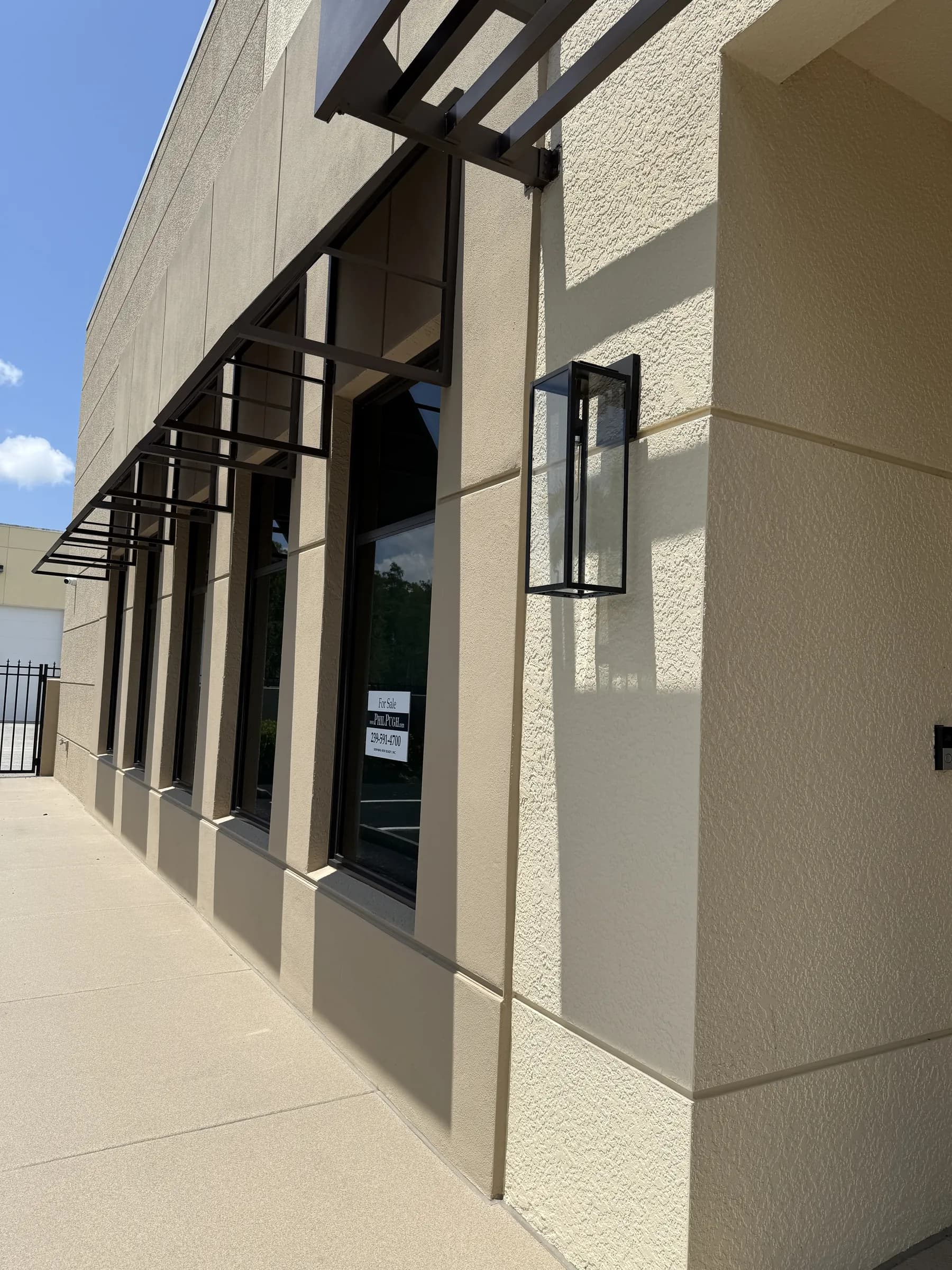 Looking back along the office wall from the far corner, a black lantern sconce in the foreground and awnings beyond.