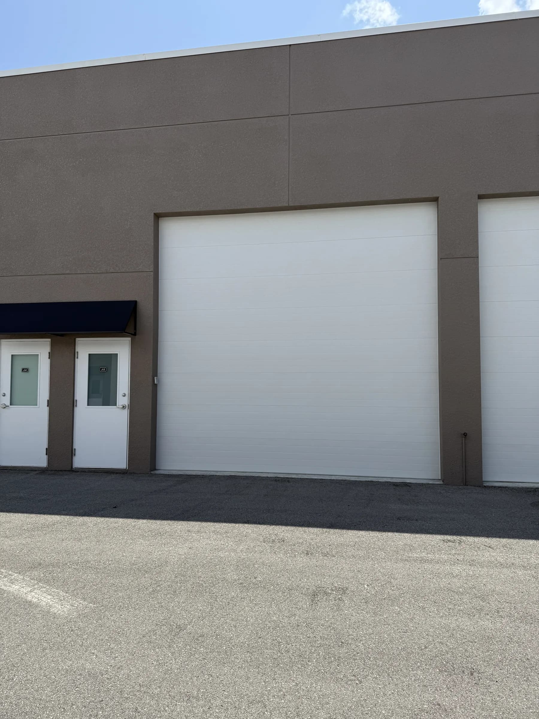 Straight-on exterior of a tall white sectional garage door with two adjacent side doors under a navy awning.