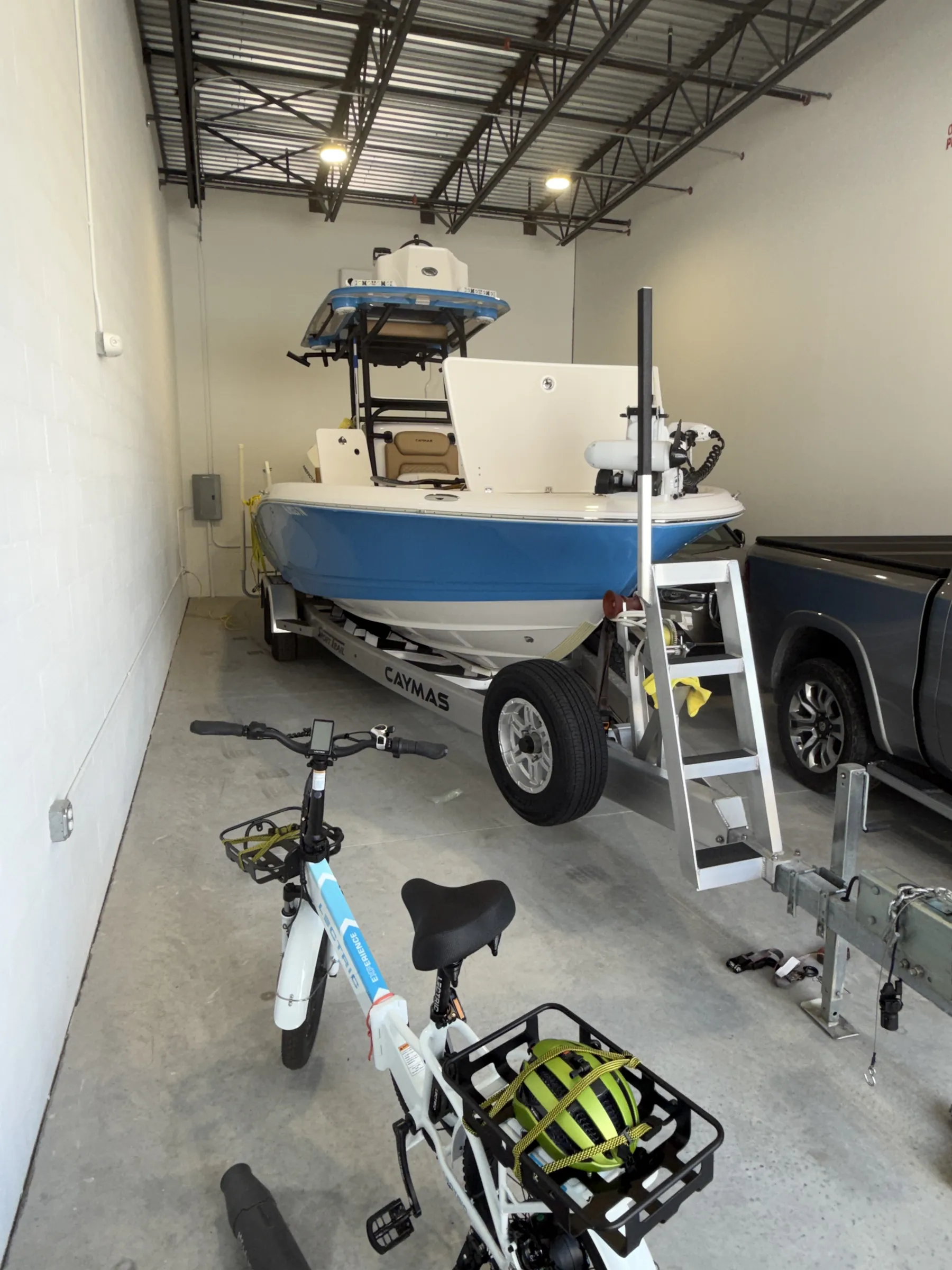 Interior along the side wall — a trailered blue boat with a boarding ladder, a folding e-bike in the foreground and a truck bed at right.