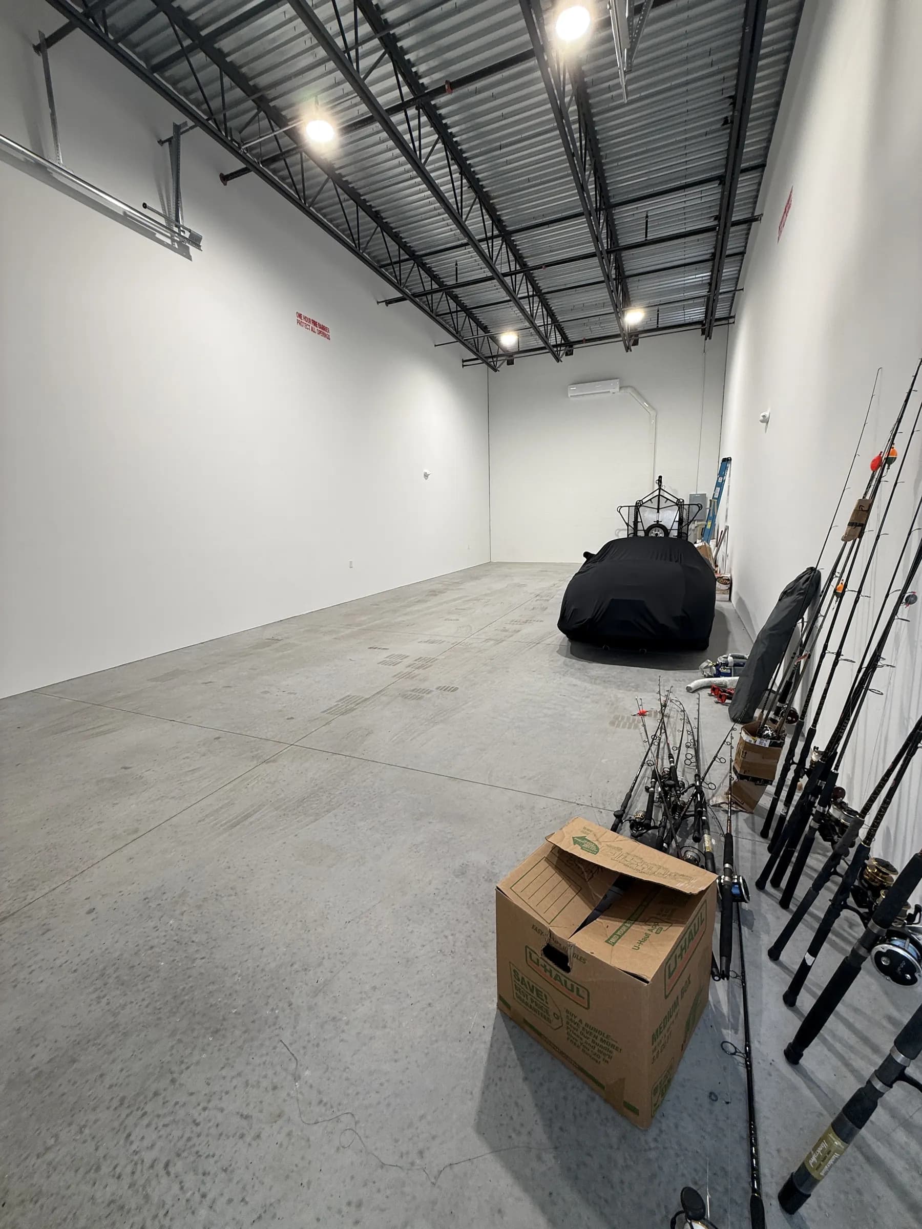 A tall unit interior with white walls, exposed steel joists and lighting, smooth concrete floor and a covered vehicle at the rear.