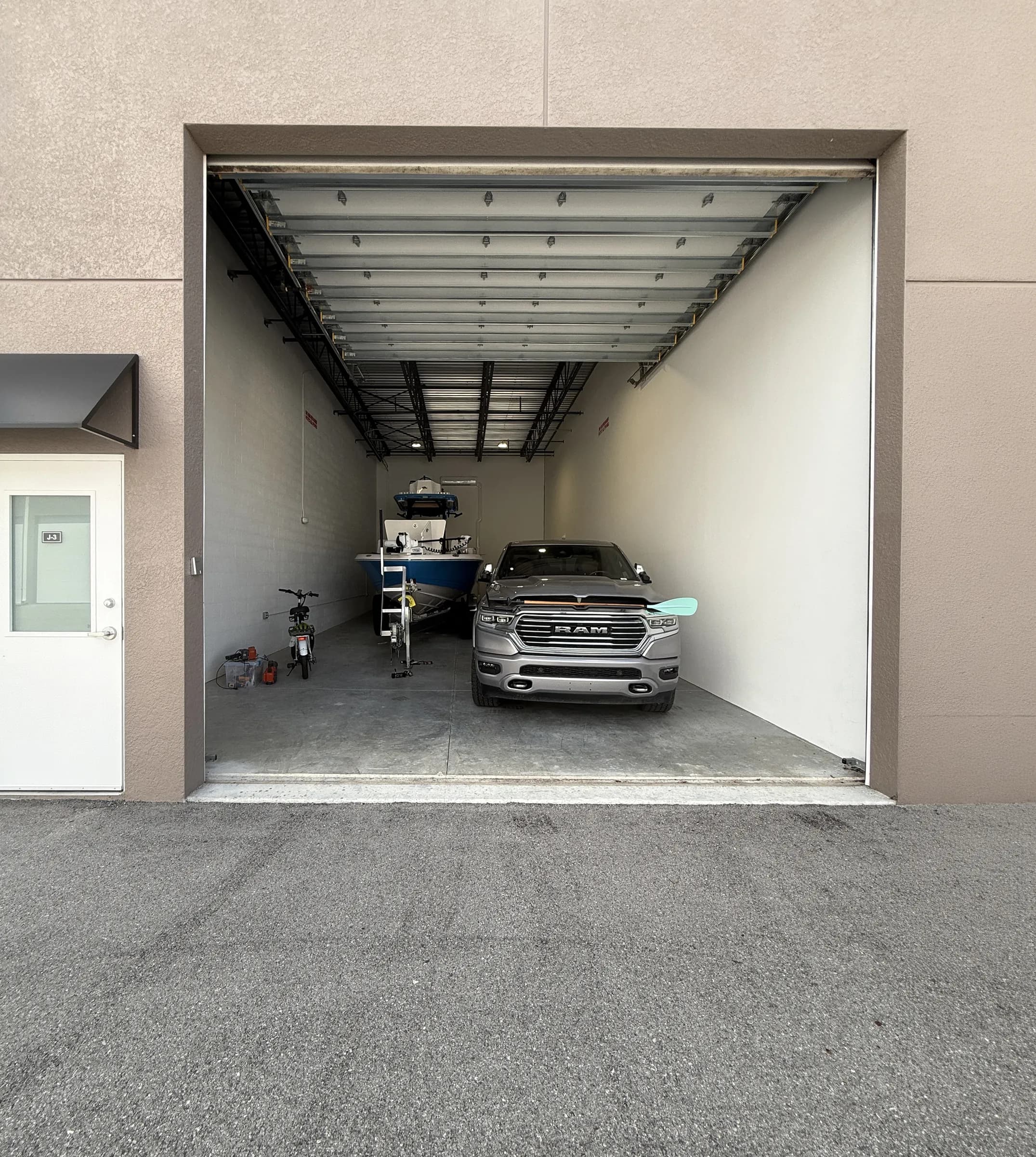 View from the drive aisle through a wide open garage door into a deep unit holding a pickup, a trailered center-console boat and a bicycle.