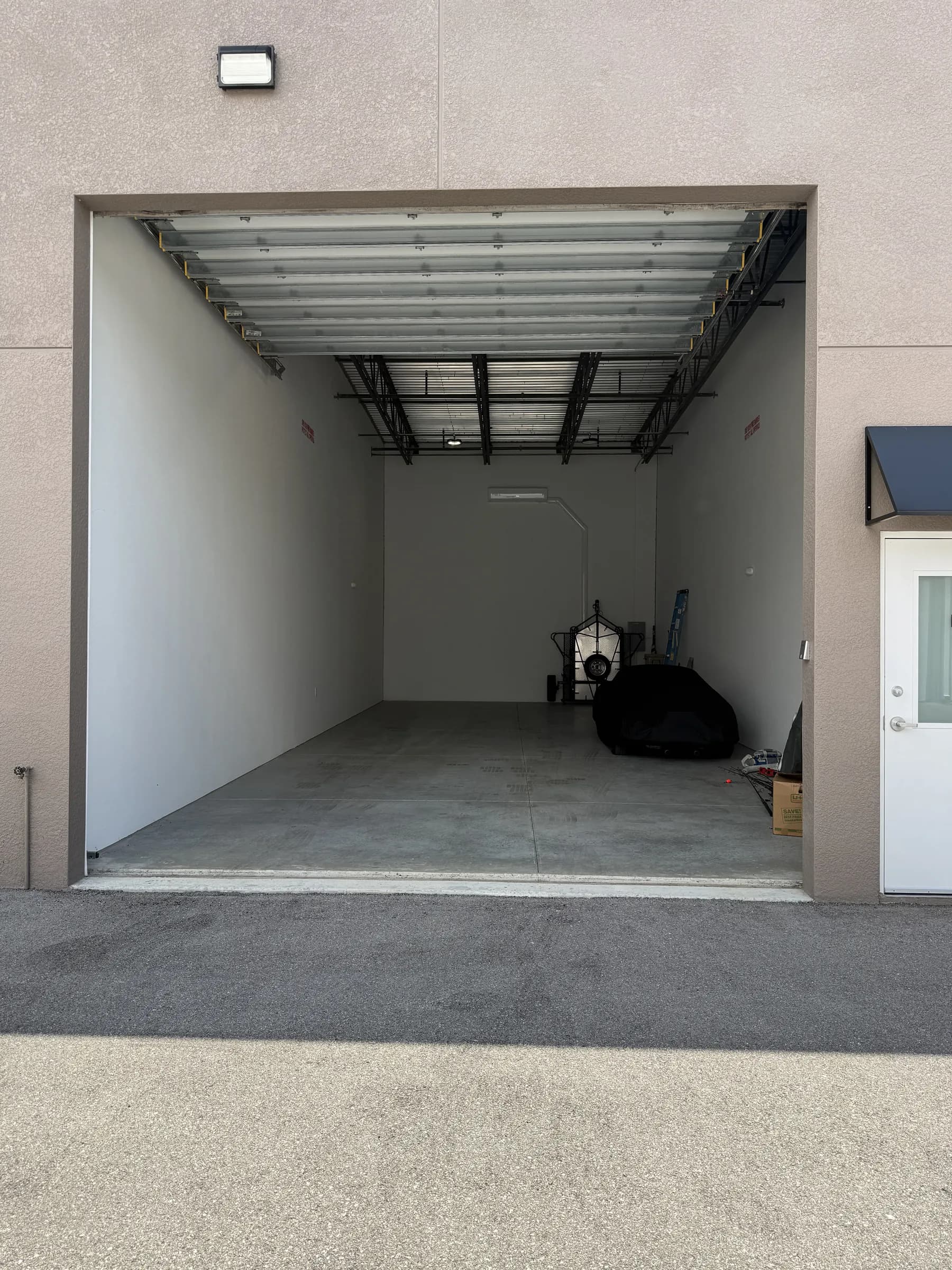 View from the drive aisle through an open overhead door into a unit, showing the raised door panels, steel roof structure and covered vehicle inside.