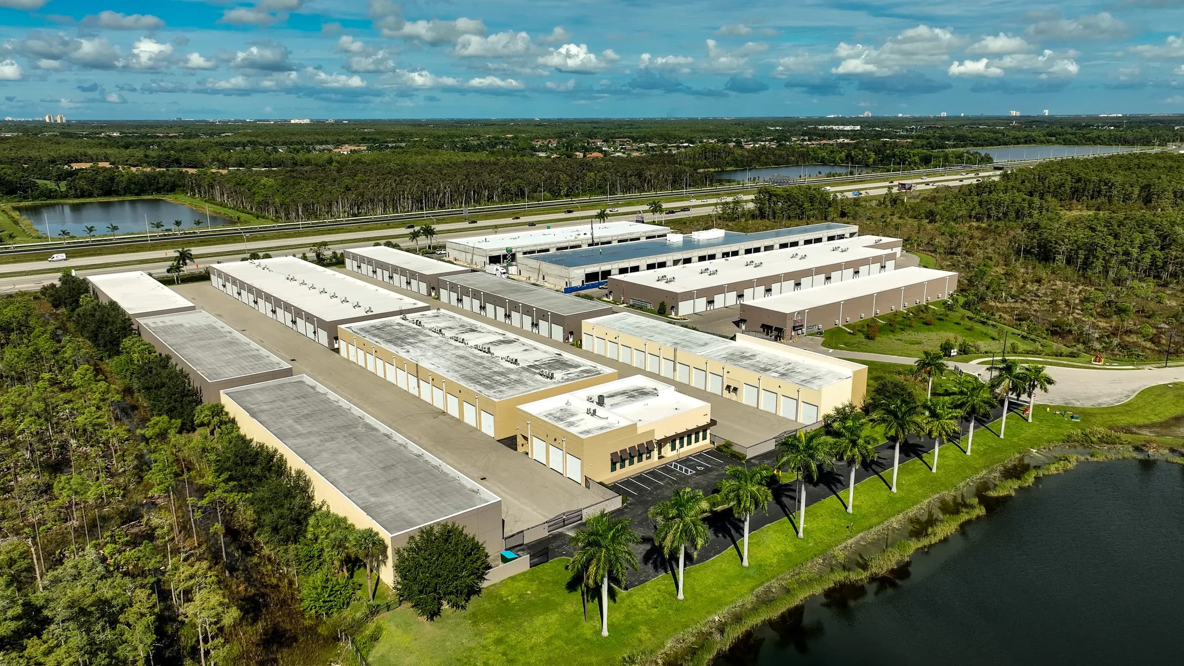 Aerial view across the lake and the palm-lined entrance toward the Vehicle Fortress campus, with I-75 behind.