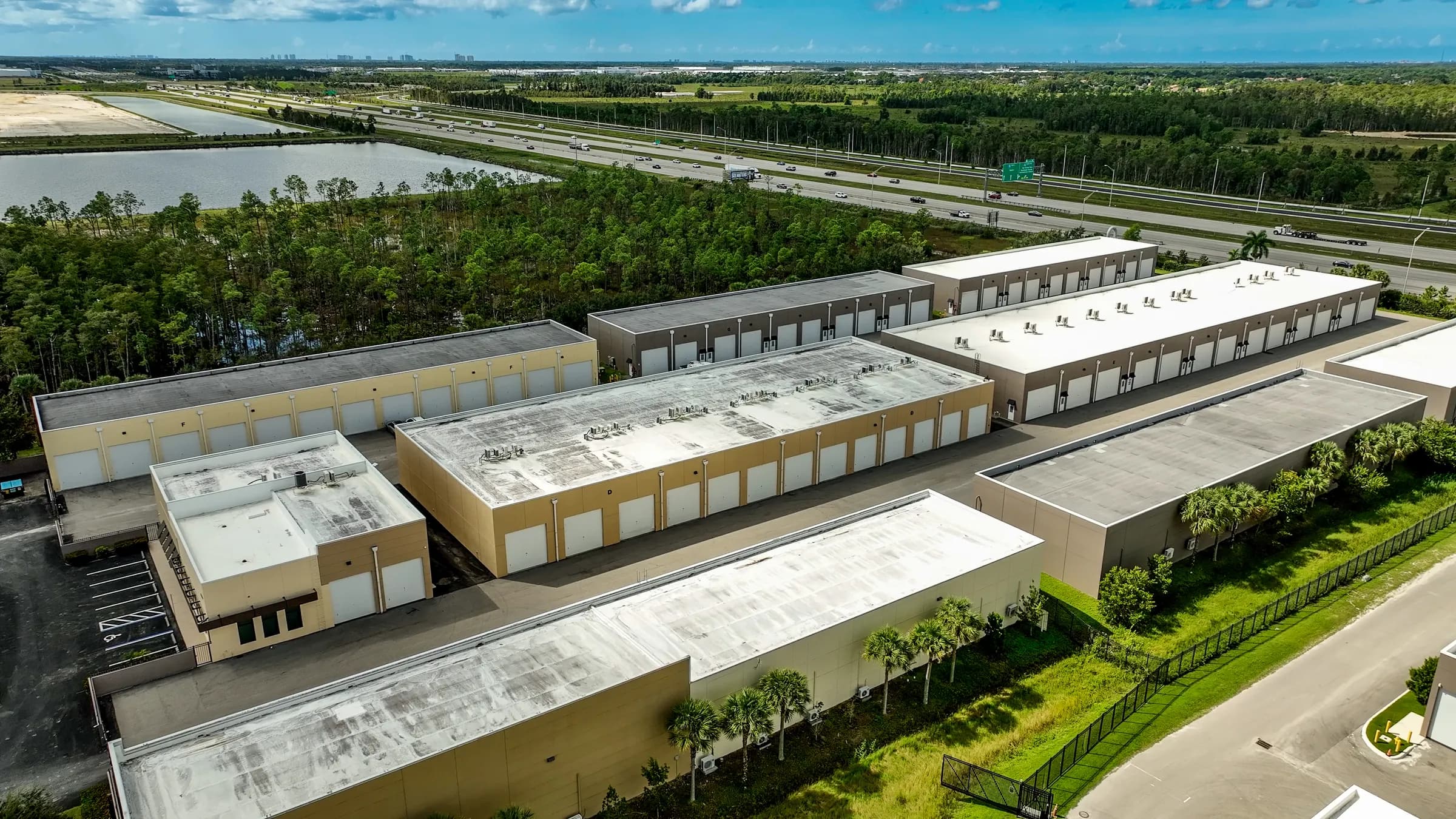 Close aerial over the rooftops and rows of garage doors, with the interstate and a lake behind.