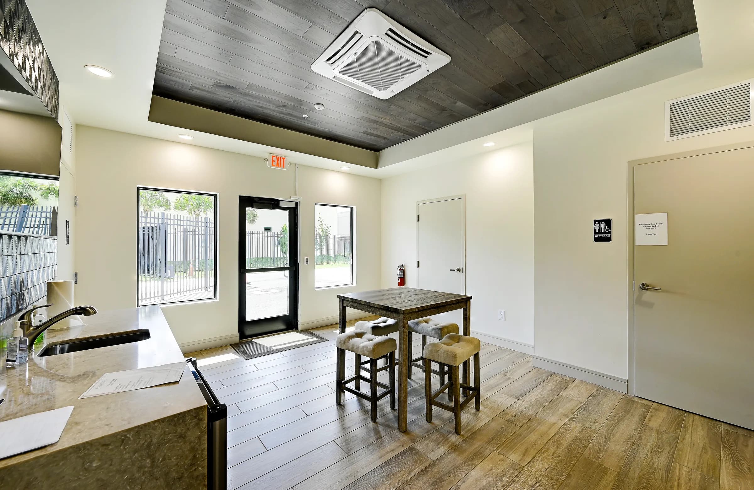 The common room seen from the counter, with the high-top table, windows and the glass entry door.