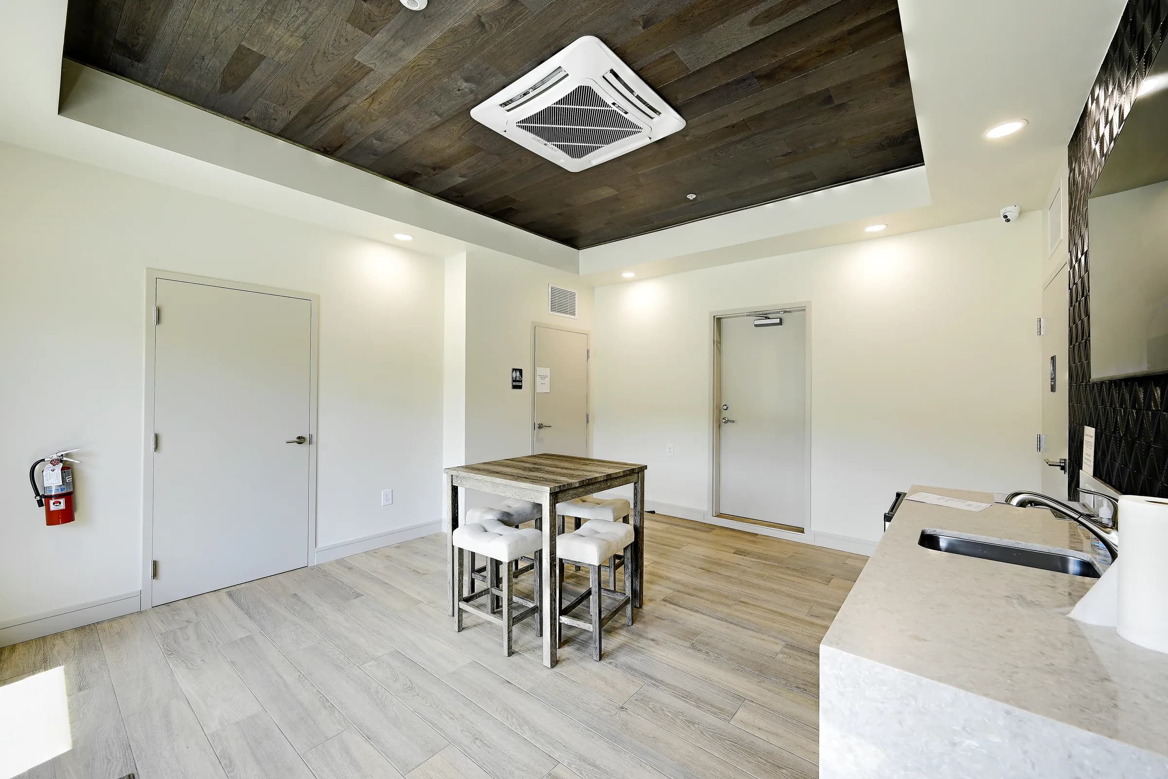 The common room under its wood-plank tray ceiling, with the high-top table, stools and quartz counter sink.