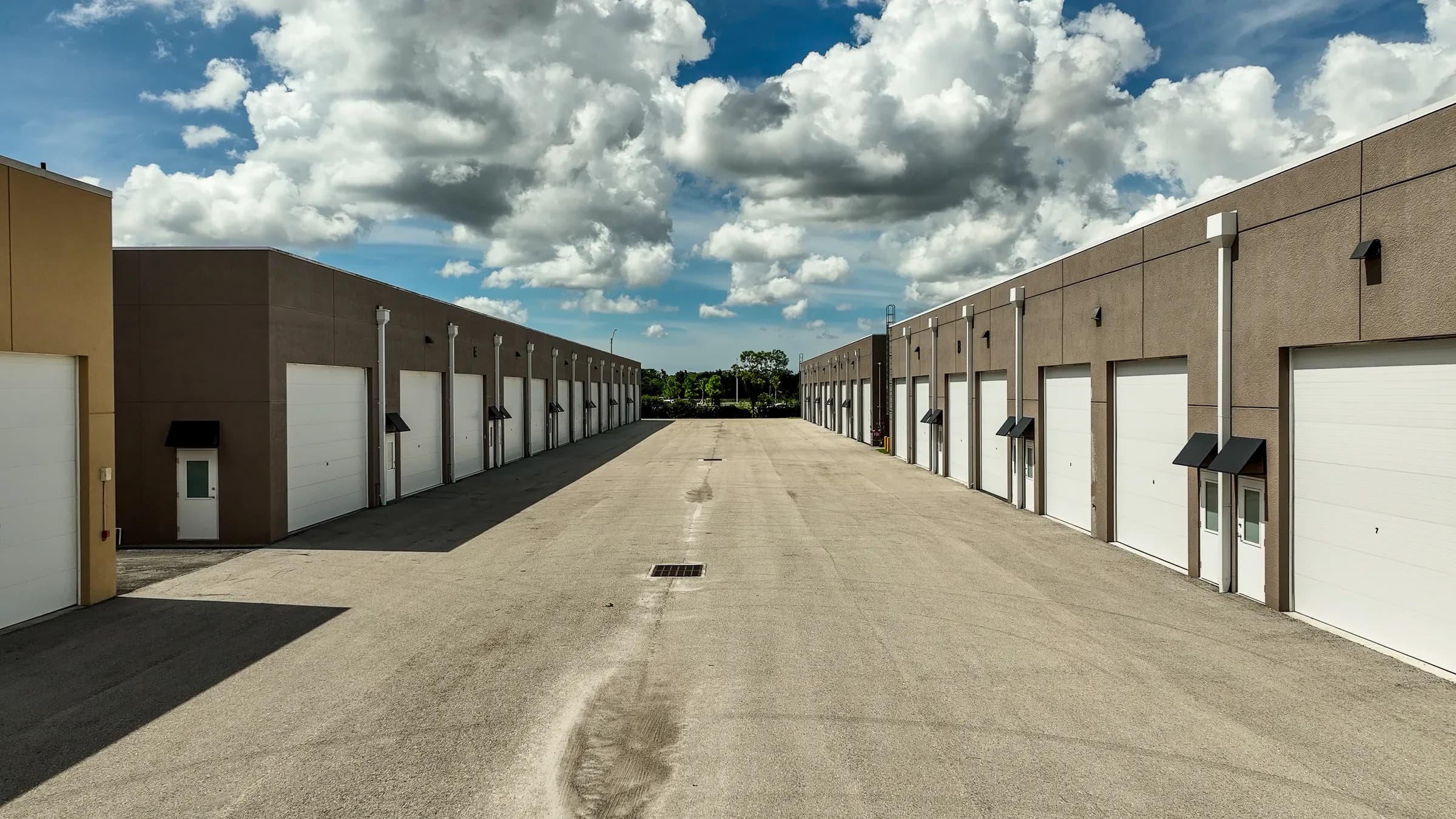 Low drone view down a 65 ft drive aisle between two Vehicle Fortress buildings, with large clouds above.