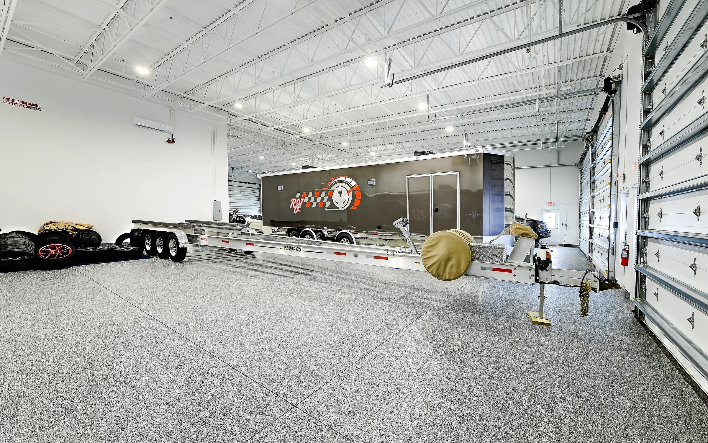 A large Vehicle Fortress unit holding a race car hauler trailer and an open car trailer, with tall sectional garage doors