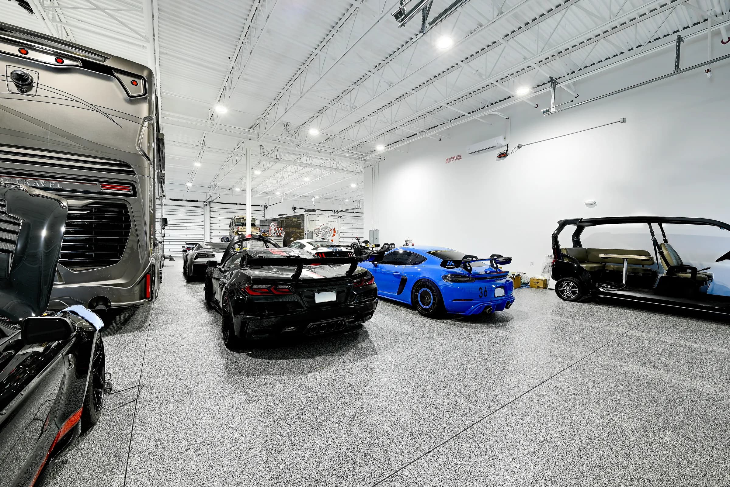 A large unit with a motor coach, a black supercar and a blue sports car on the epoxy floor.