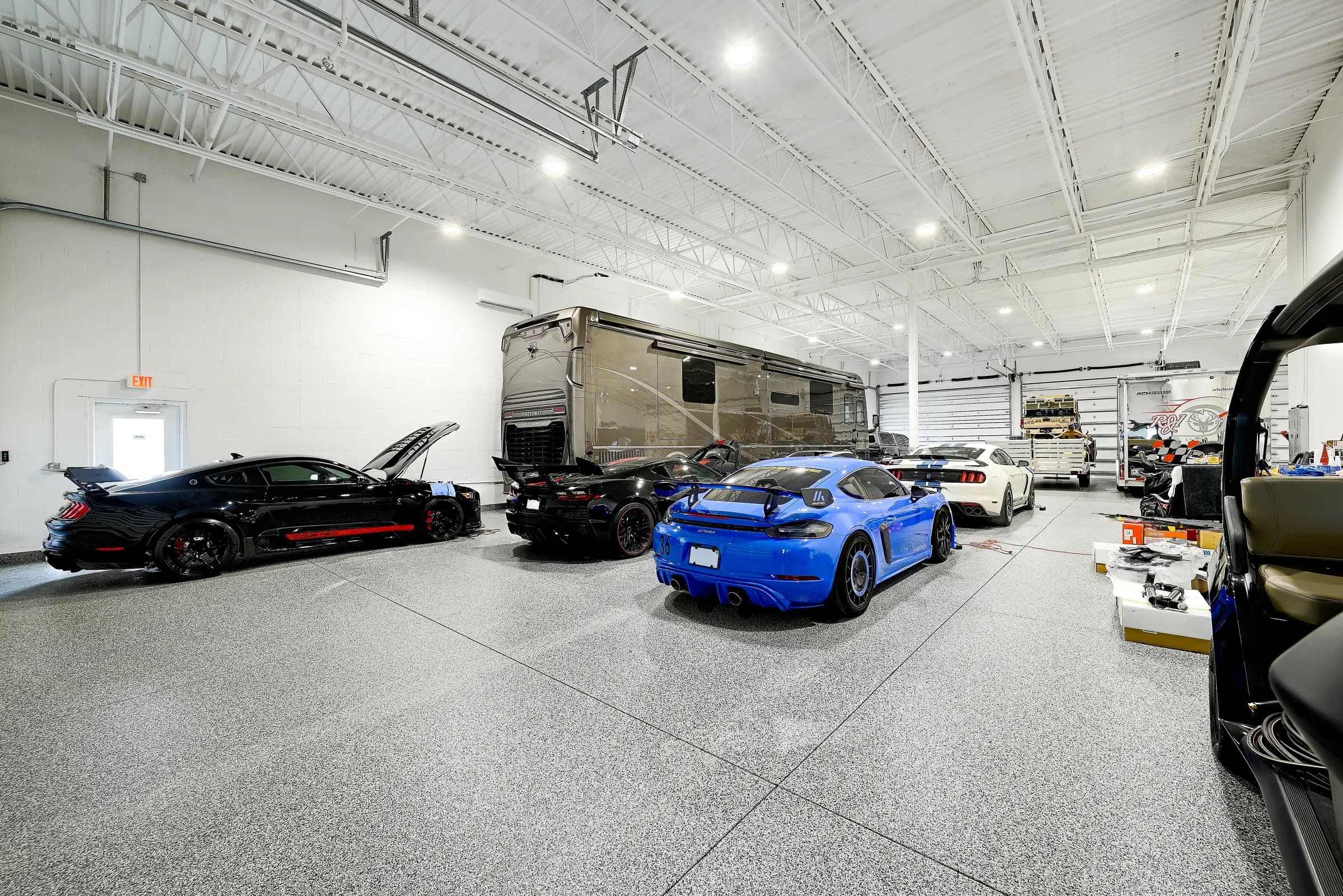 A motor coach parked alongside sports cars inside a large Vehicle Fortress unit