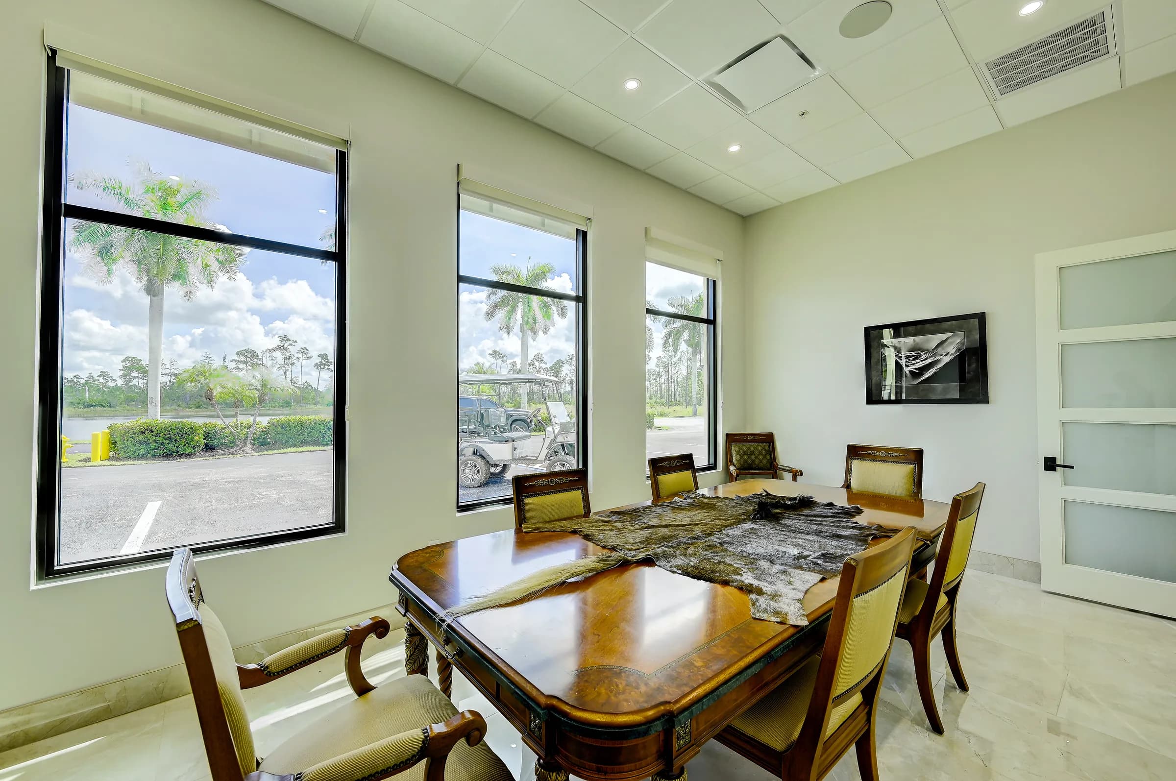 The showroom's finished conference room with a wood table and upholstered chairs, large windows looking out to palms and the lot.