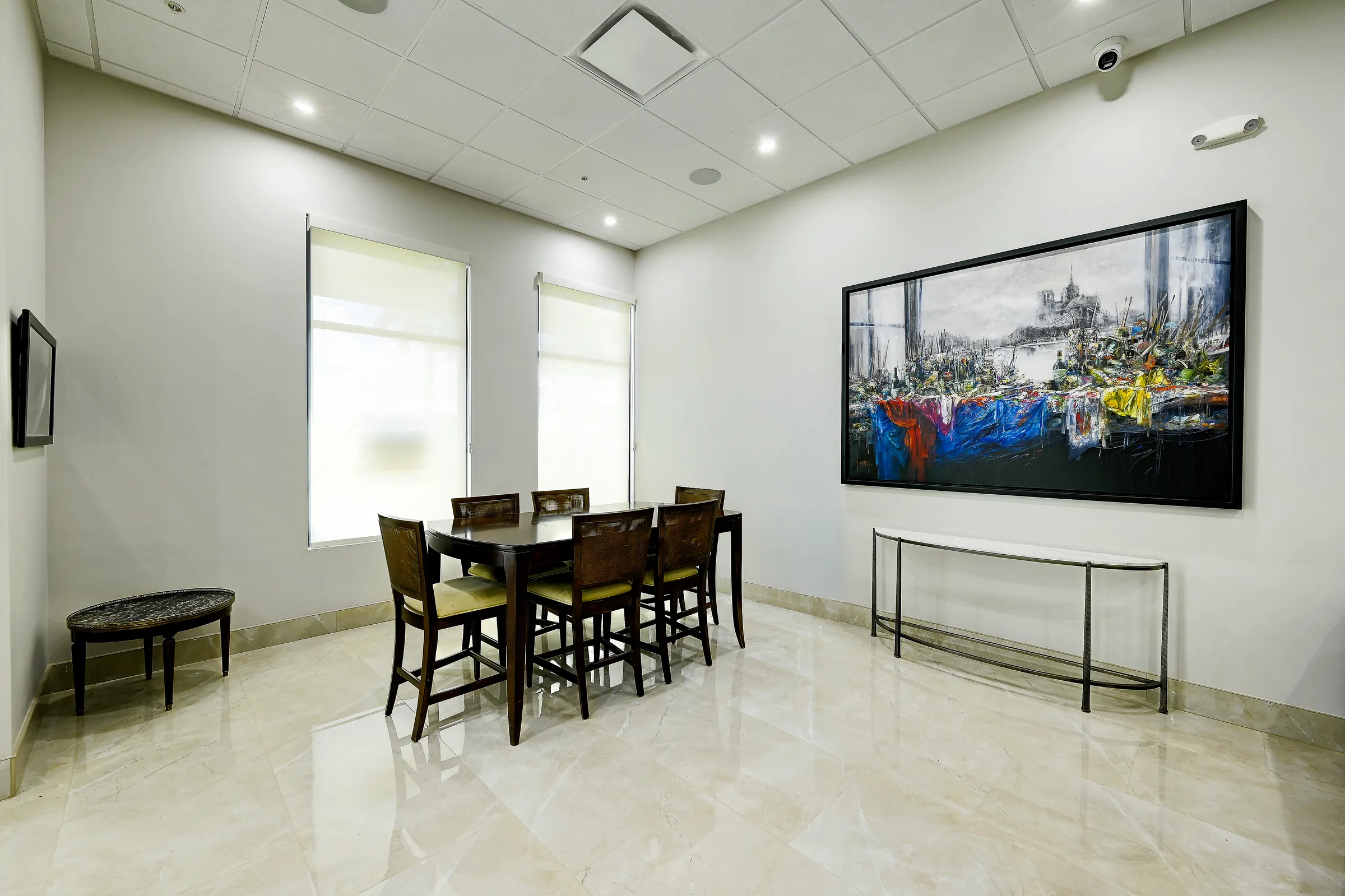 The showroom's dining area with a dark wood table, a large painting and a marble-look floor.