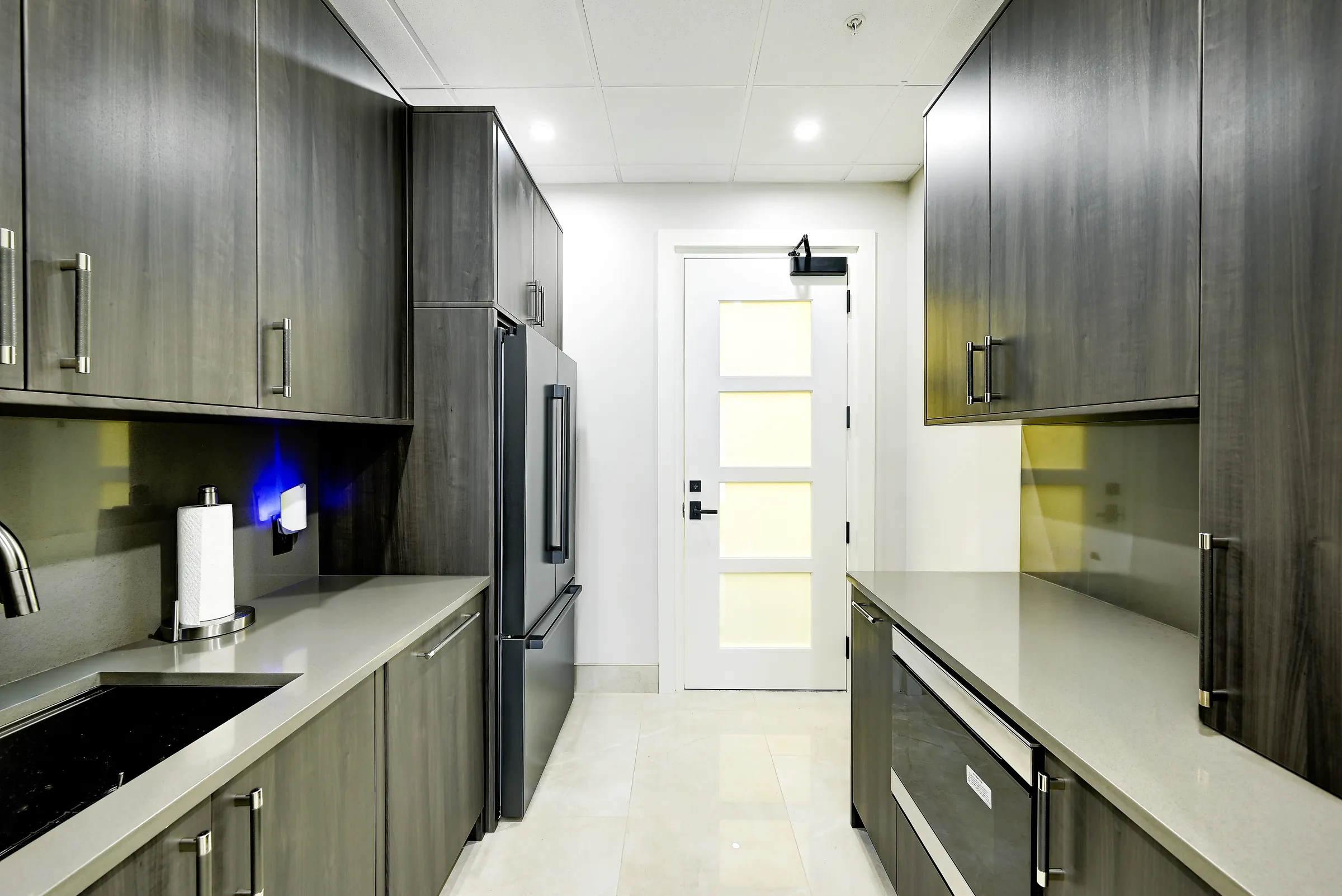 The showroom's galley kitchen with dark wood cabinets, quartz counters and a refrigerator.