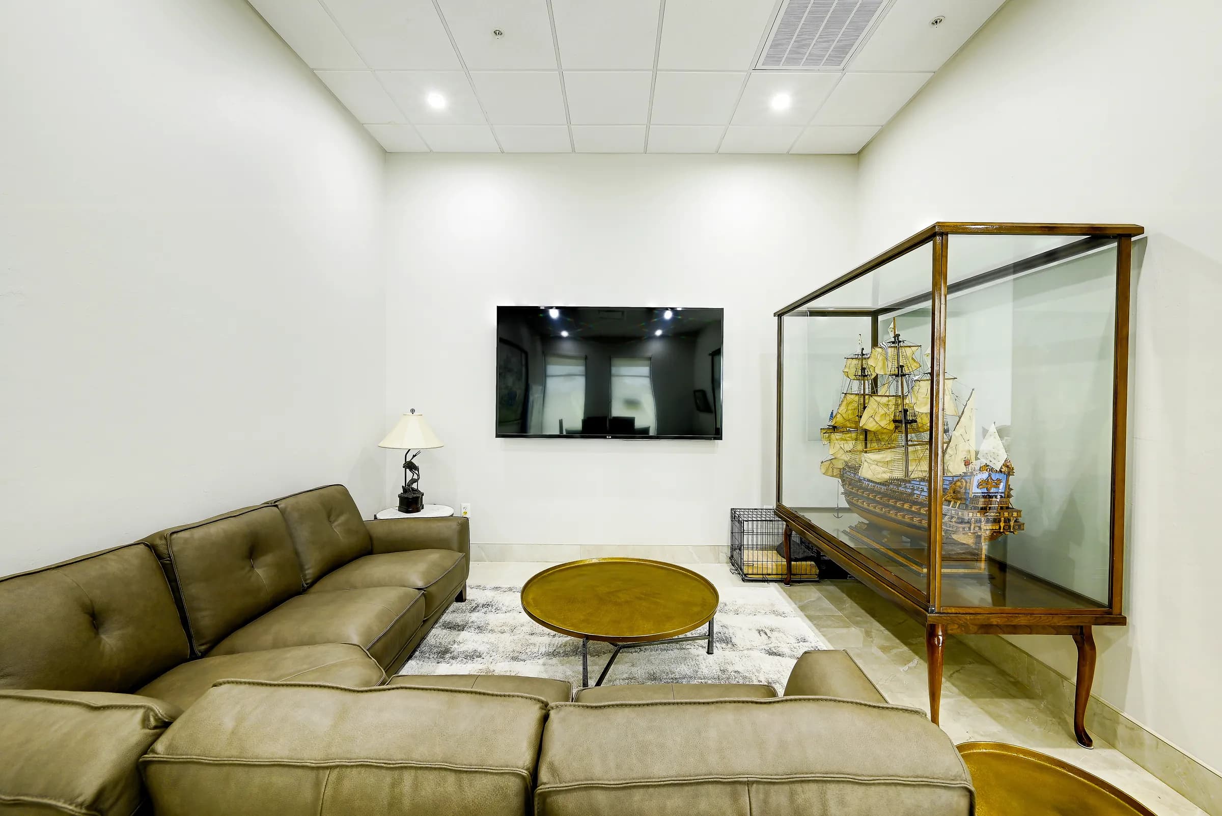 The showroom's living area with a leather sectional, round coffee table, TV and a model ship in a glass case.