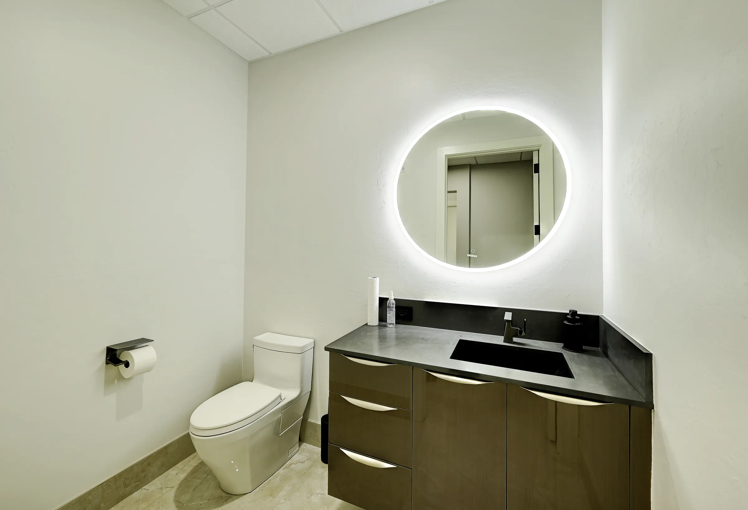 The showroom's powder room with a backlit round mirror, floating vanity and toilet.