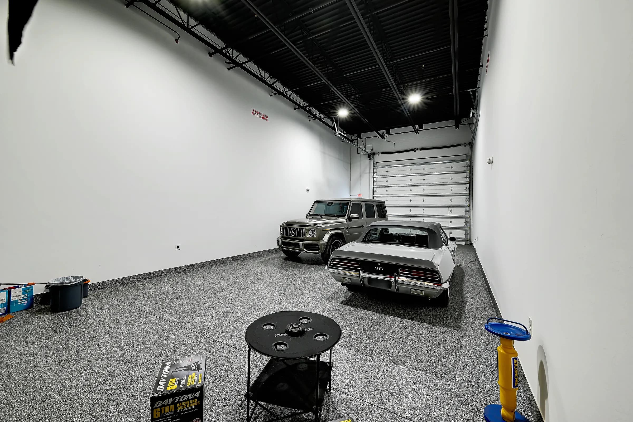 A unit with a black ceiling, a silver classic muscle car and a luxury SUV near the rear door.