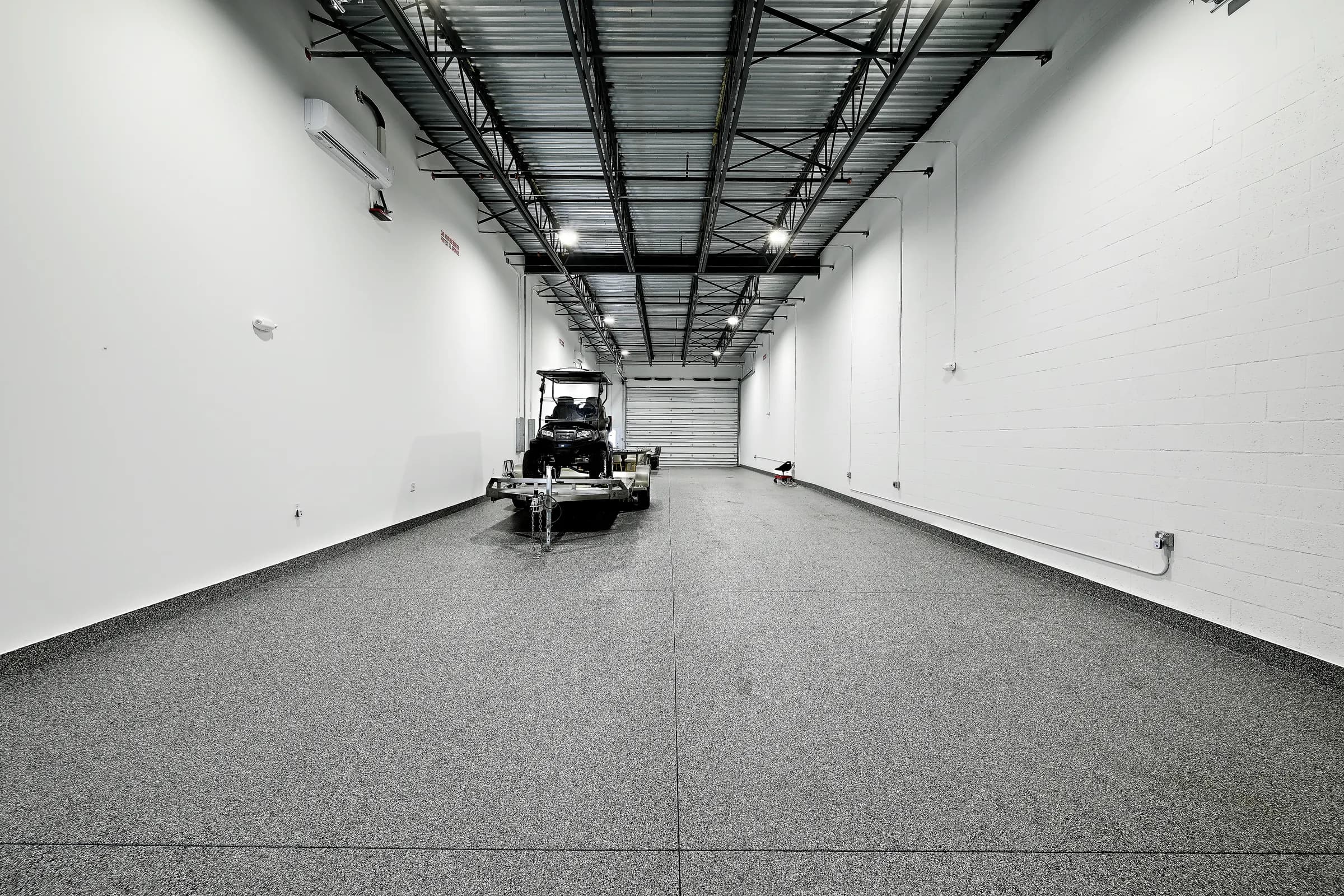 A long finished unit with speckled epoxy floor, white walls, open steel trusses and a utility vehicle on a trailer at the back.