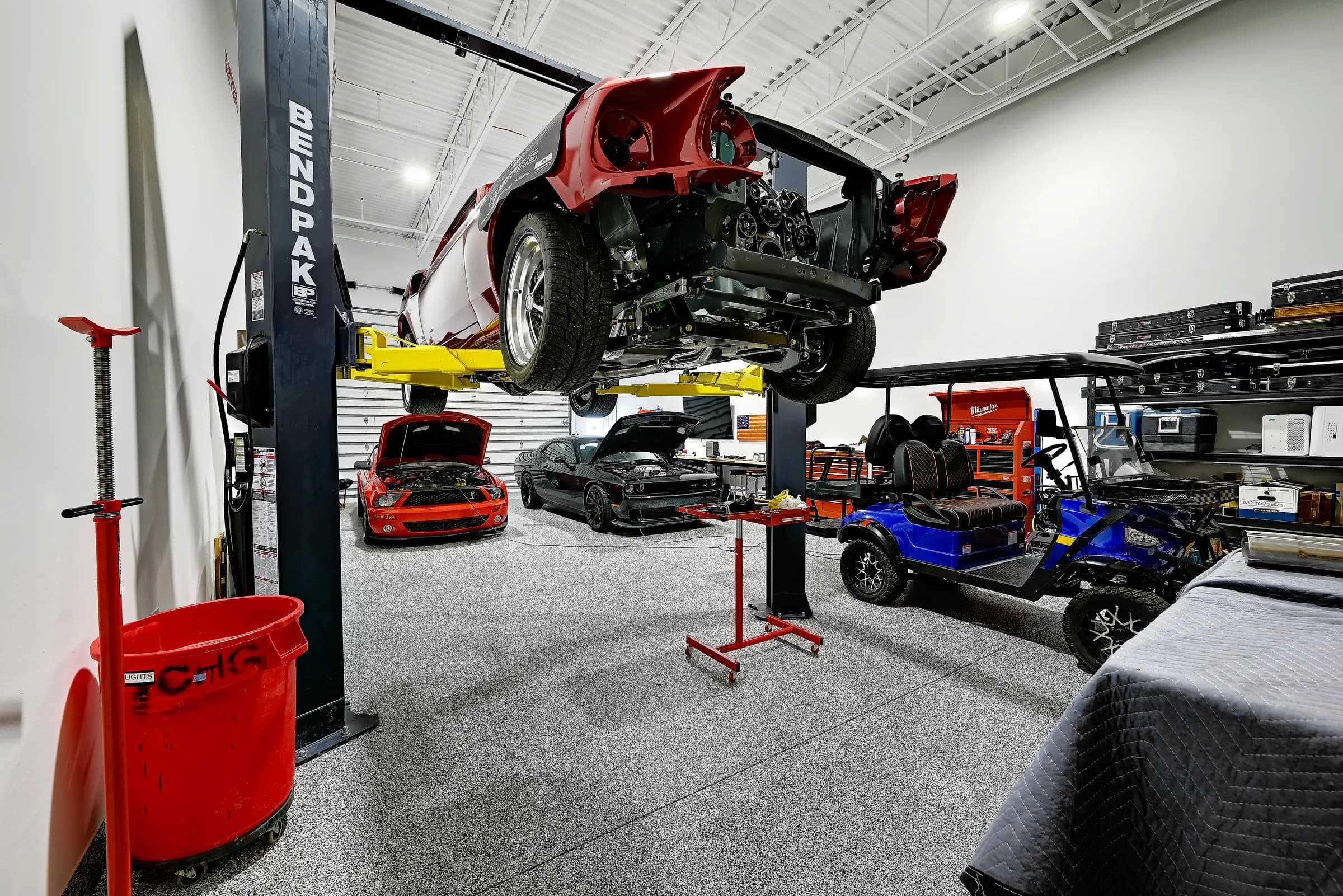 An owner's unit with a car raised on a two-post lift, a golf cart and rolling tool chests.