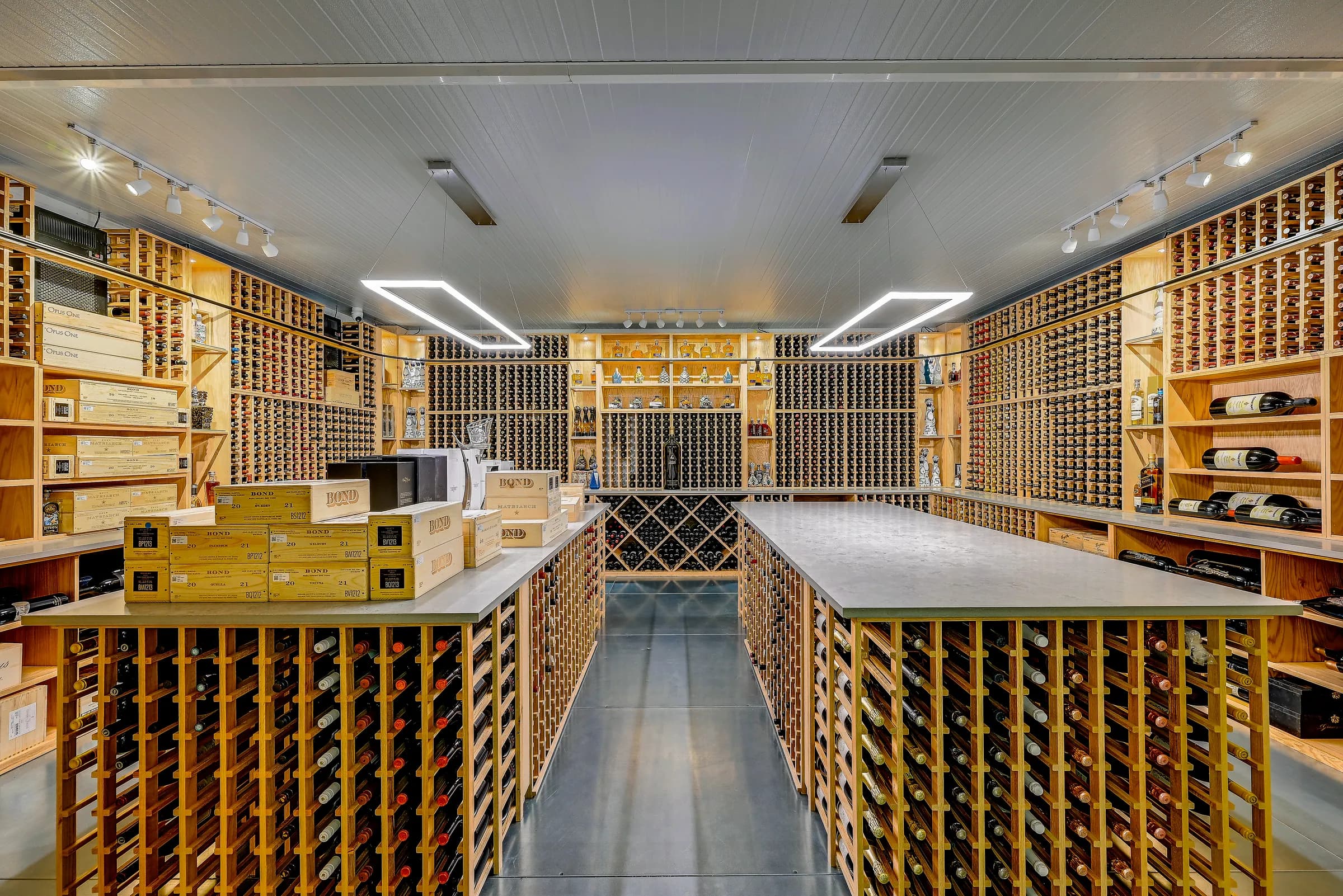 Straight view down the center of the wine cellar between two rack islands, under track lights.