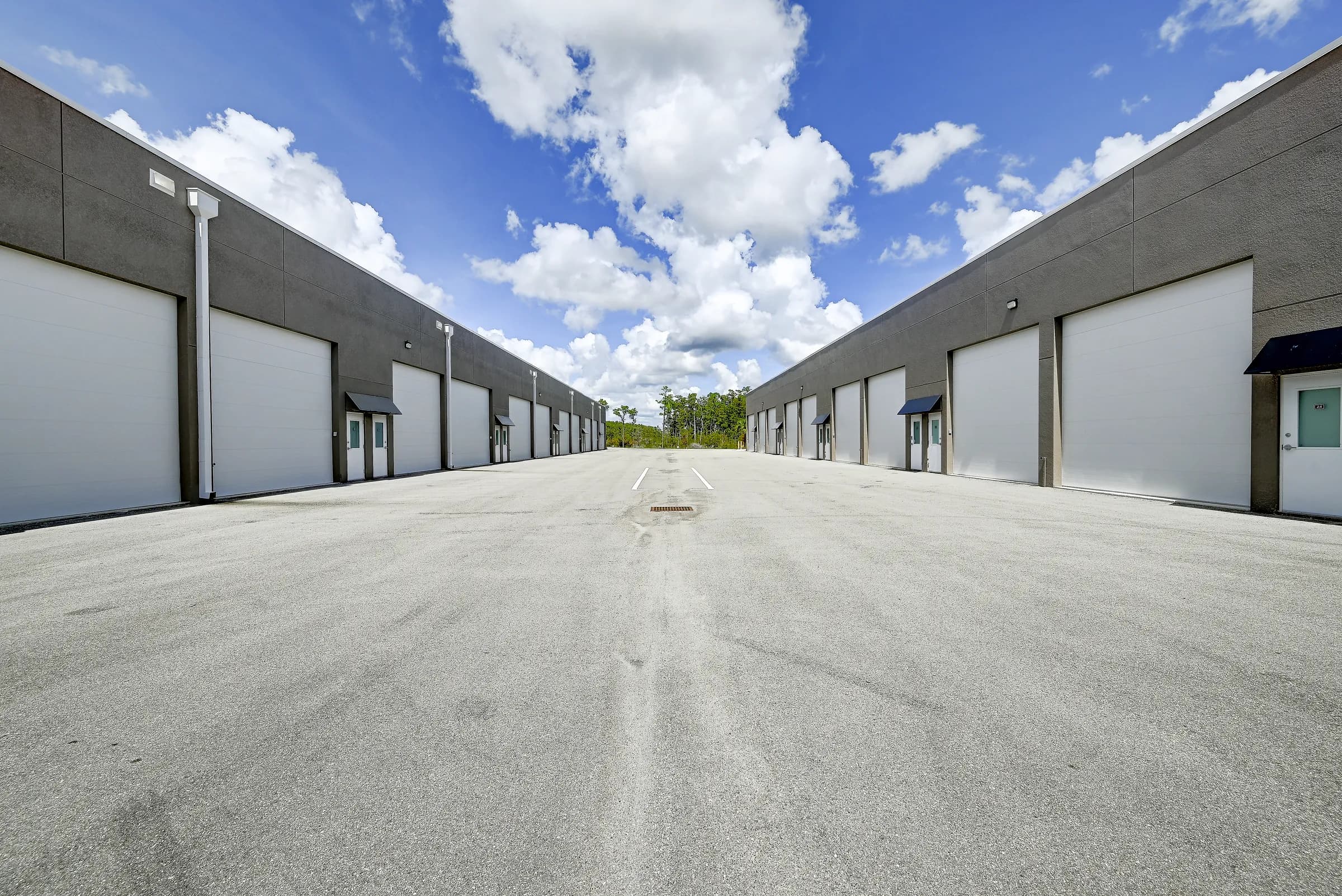 Ground-level view down a 65 ft drive aisle between two rows of tall white garage doors at Vehicle Fortress.